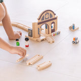 Child making a railroad setup using rail pieces and a PlanToys train station
