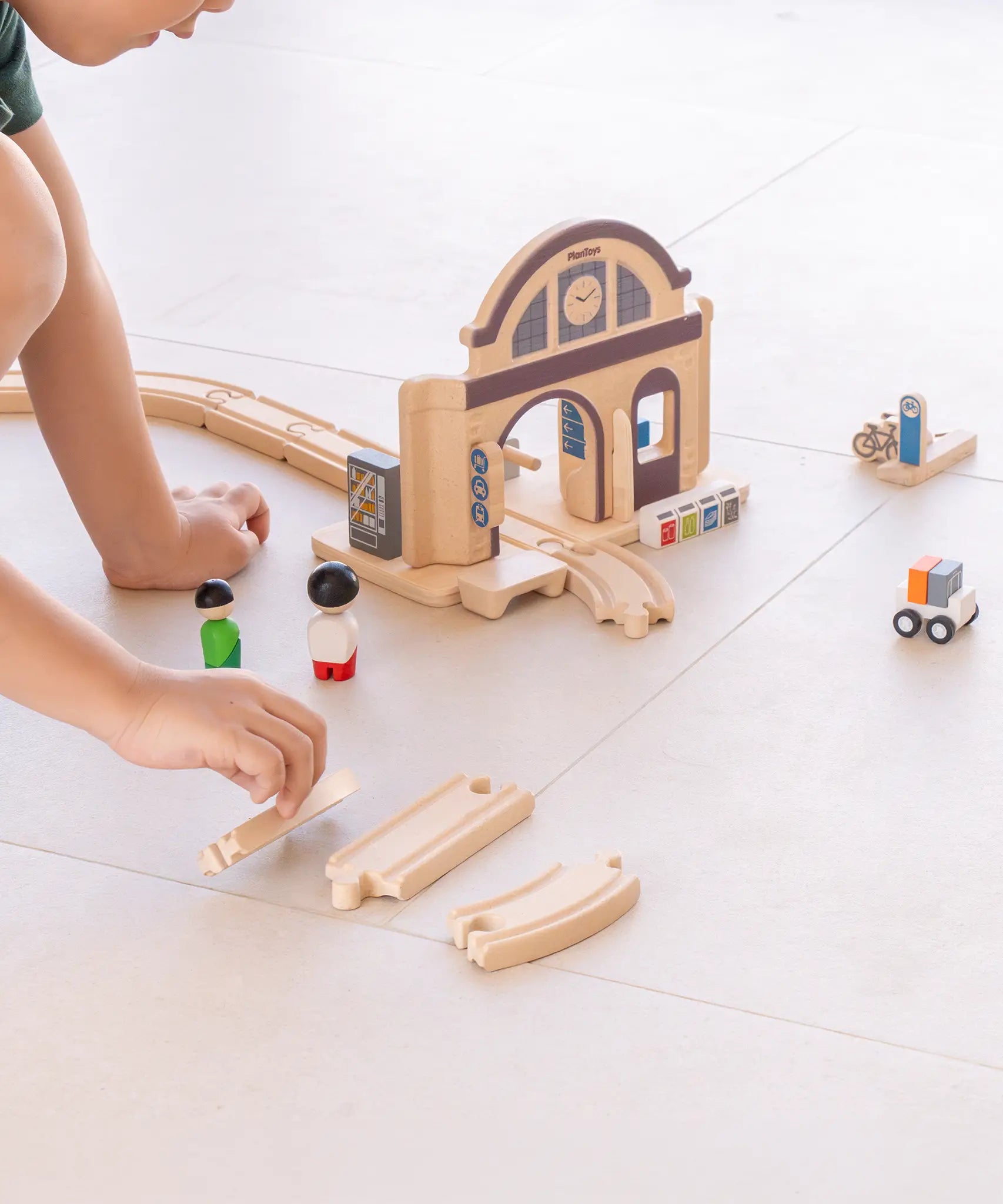 Child making a railroad setup using rail pieces and a PlanToys train station