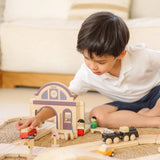 Child playing with a railroad setup made from wooden PlanToys rail pieces and the train station.