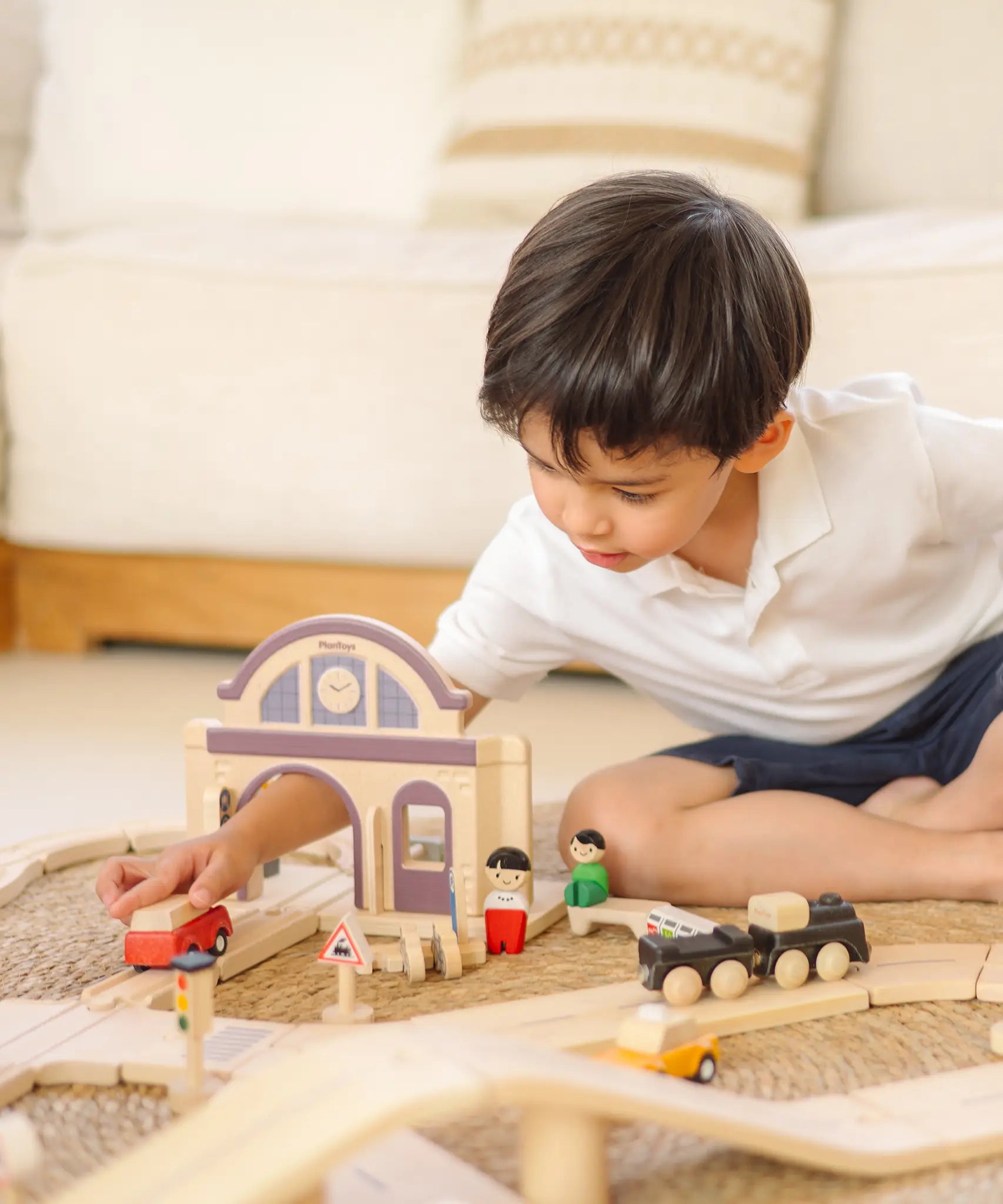 Child playing with a railroad setup made from wooden PlanToys rail pieces and the train station.