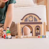 PlanToys wooden train station showing a child holding a wooden figure sitting on a suitcase trolley