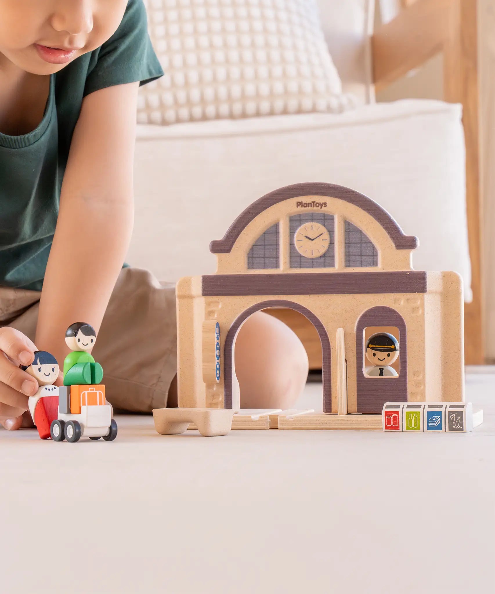 PlanToys wooden train station showing a child holding a wooden figure sitting on a suitcase trolley