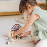 Child holding a train on wooden rails underneath a PlanToys train station 