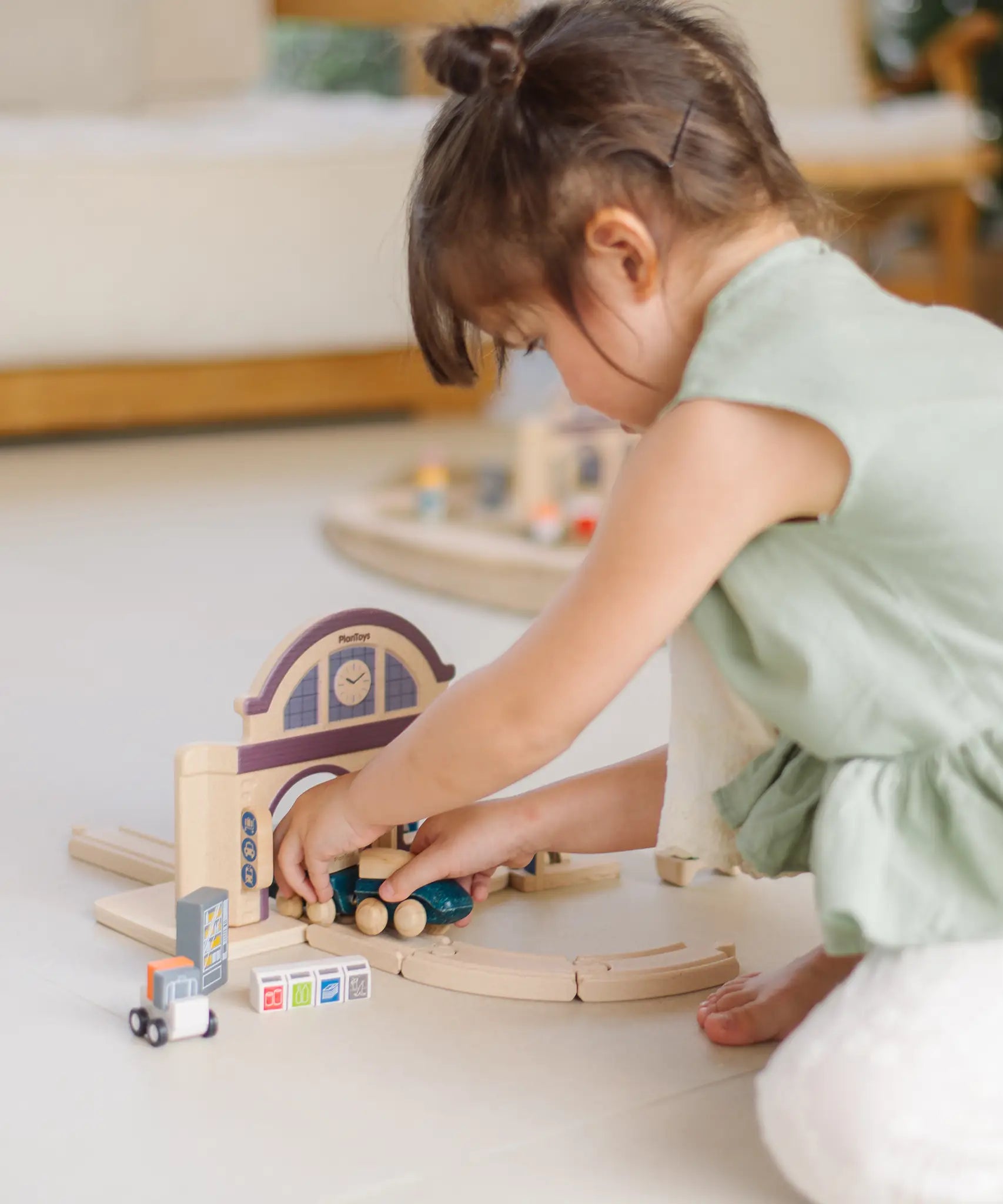 Child holding a train on wooden rails underneath a PlanToys train station 