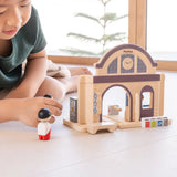 Child holding wooden people figures next to a PlanToys train station 