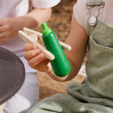 Child holding a wooden courgette with tongs from the PlanToys vegetables set