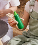 Child holding a wooden courgette with tongs from the PlanToys vegetables set