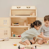 Children playing with small wooden furniture and dolls with a PlanToys Victorian dolls house in the background.