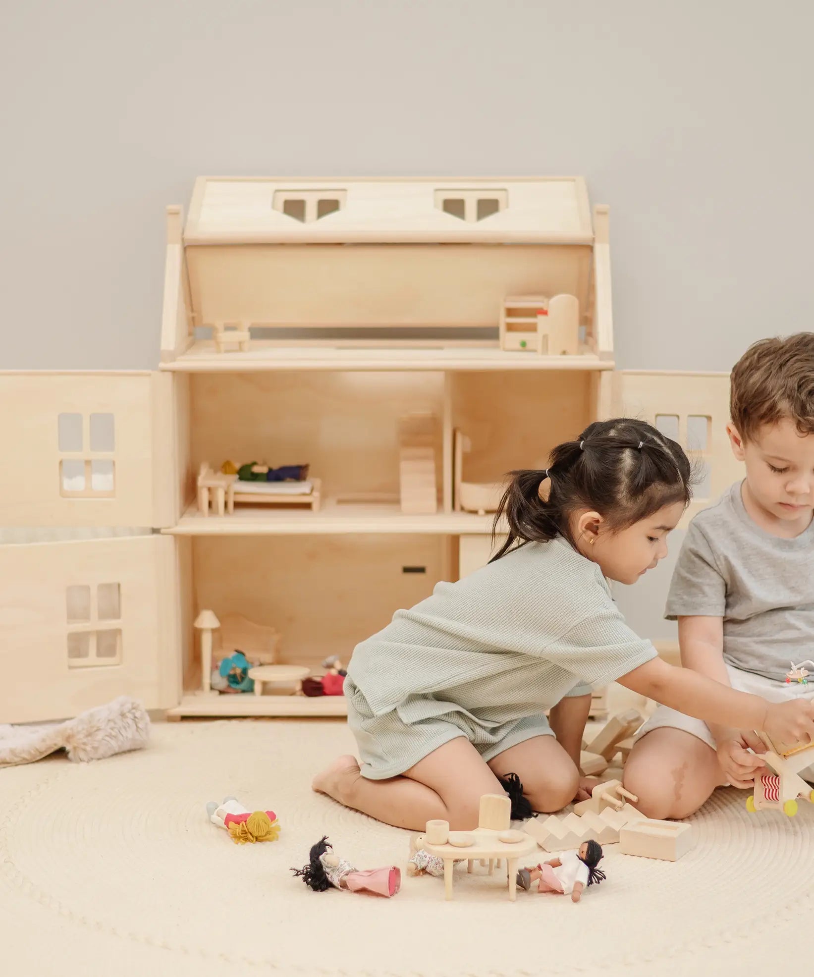 Children playing with small wooden furniture and dolls with a PlanToys Victorian dolls house in the background.