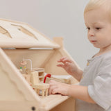 Child standing near a PlanToys Victorian dolls house showing the attic filled with furniture 