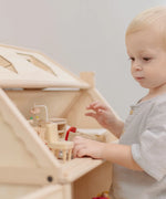 Child standing near a PlanToys Victorian dolls house showing the attic filled with furniture 