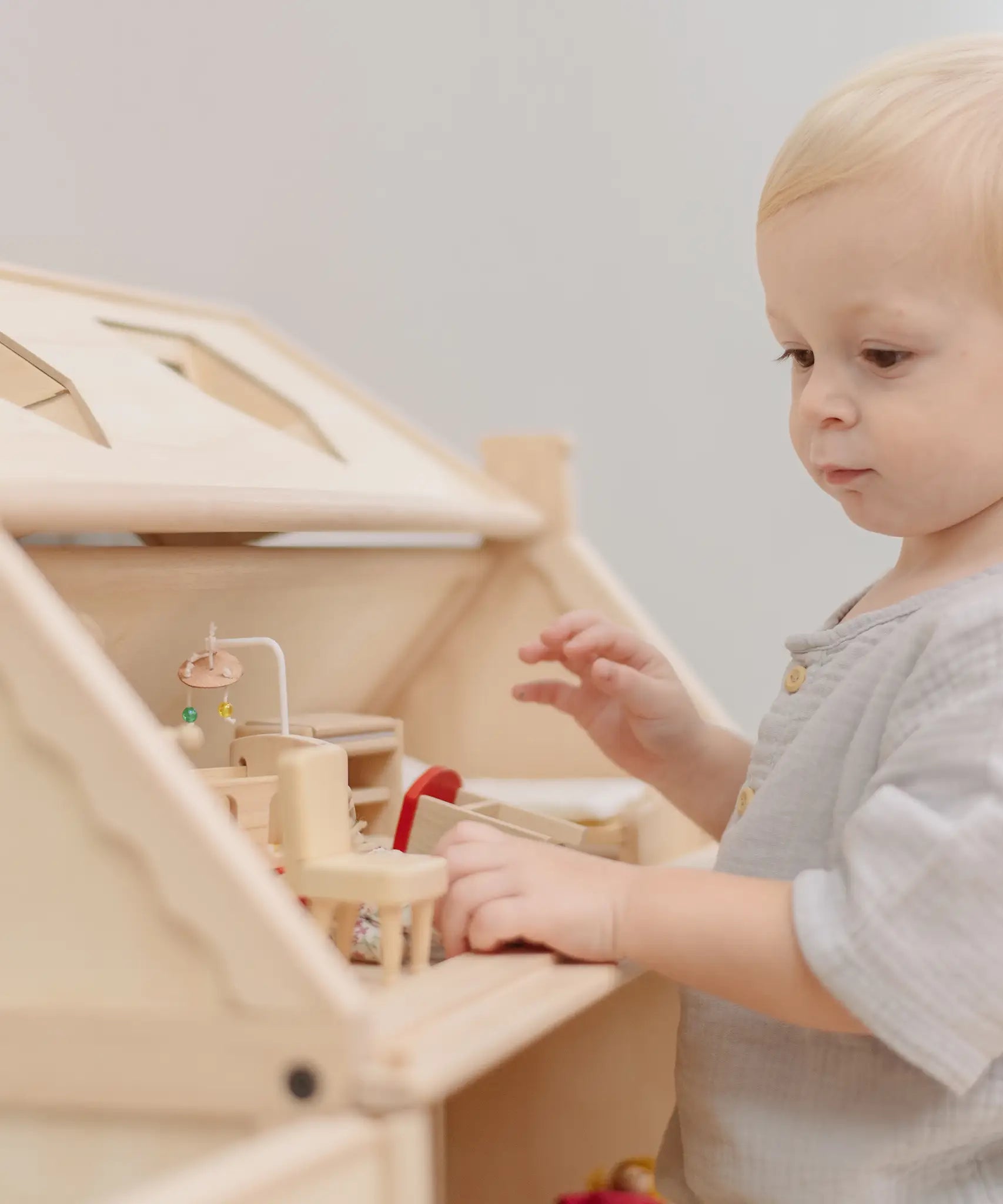 Child standing near a PlanToys Victorian dolls house showing the attic filled with furniture 