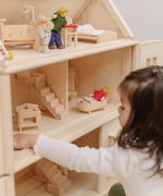 PlanToys Victorian dolls house with small furniture and dolls inside and a child sitting near