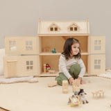 Child playing with small wooden furniture with a PlanToys Victorian dolls house in the background.