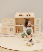 Child playing with small wooden furniture with a PlanToys Victorian dolls house in the background.