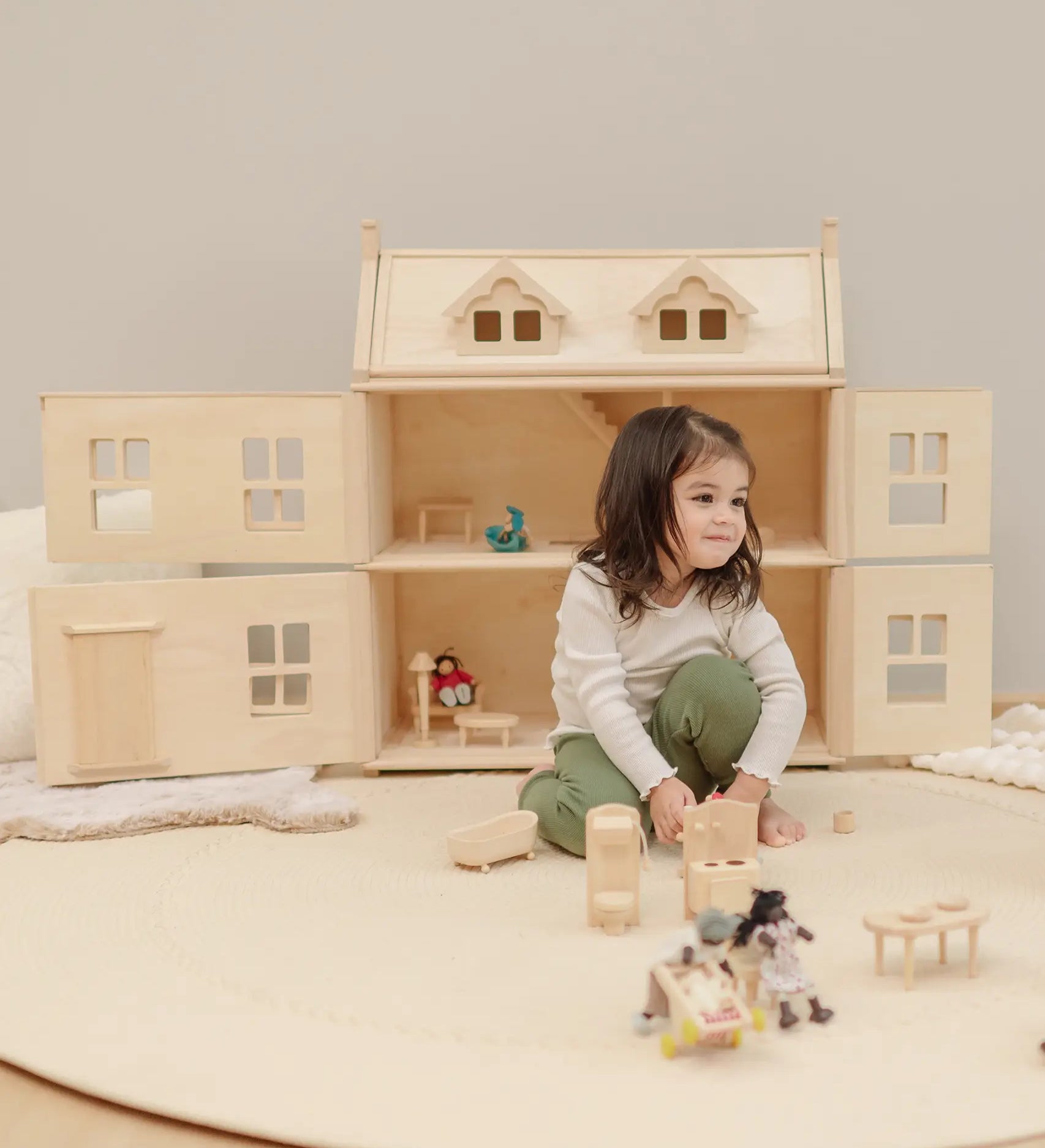 Child playing with small wooden furniture with a PlanToys Victorian dolls house in the background.