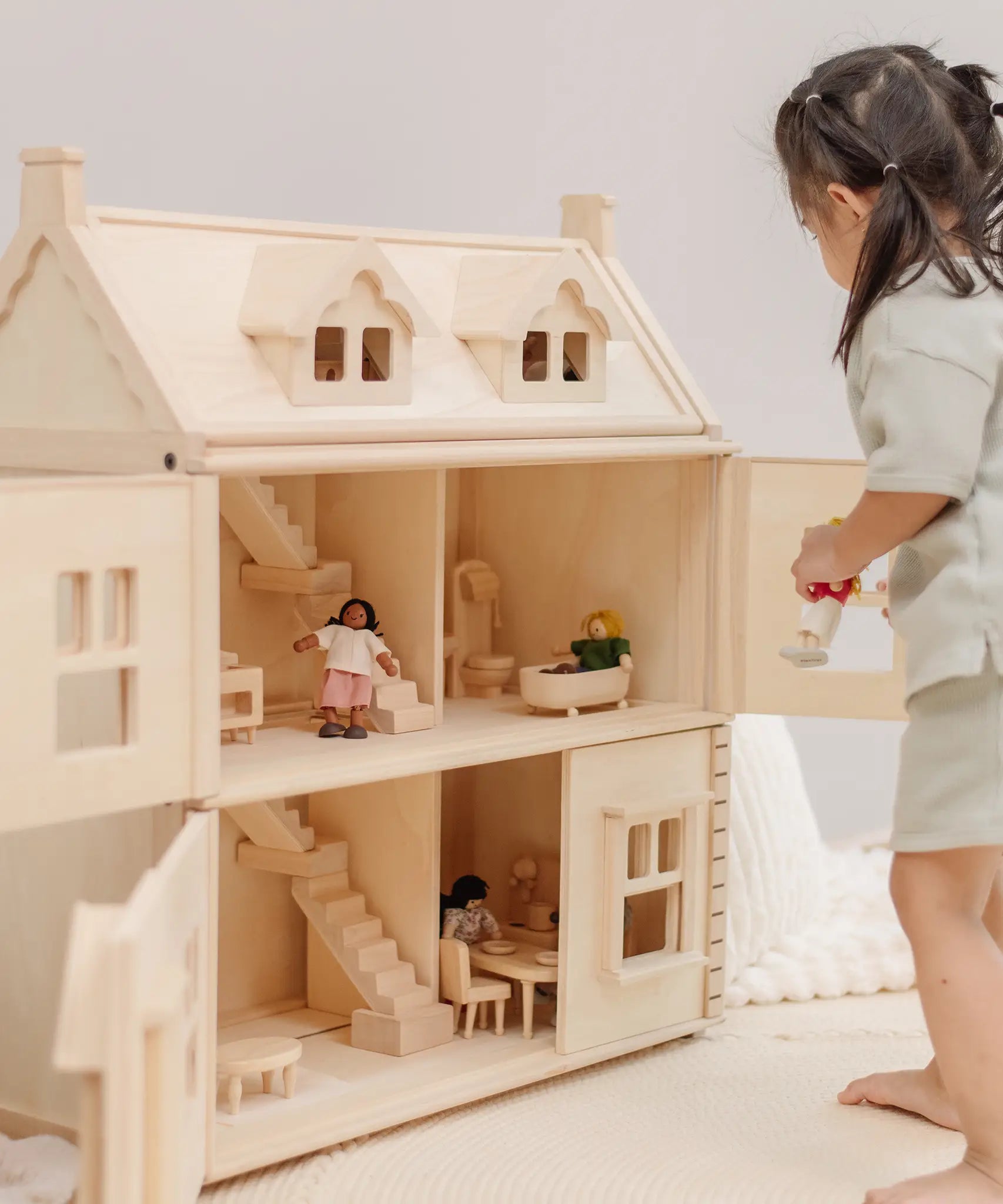 Child holding a doll next to a PlanToys wooden Victorian dolls house