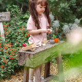 Child standing next to a bench with pieces from the PlanToys garden wheelbarrow set 