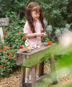 Child standing next to a bench with pieces from the PlanToys garden wheelbarrow set 