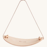 PlanToys Balance Board is a curved board made from wood, showing the natural wood grain. There is also a removable beige rope to help support balancing, which can be removed once the child feels more confident with balancing. The image is on a cream background