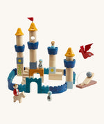 The PlanToys Castle Building Blocks in Orchard colours, made into a colourful castle display. The set comes with castle wall blocks in shades of blue, blocks to make castle towers and turrets, little people figures, a horse, a dragon and a catapult to defend the castle. The image is on a cream background