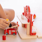 Child playing with the PlanToys fireman figure and fire engine next to the fire station.