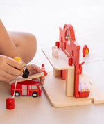 Child playing with the PlanToys fireman figure and fire engine next to the fire station.