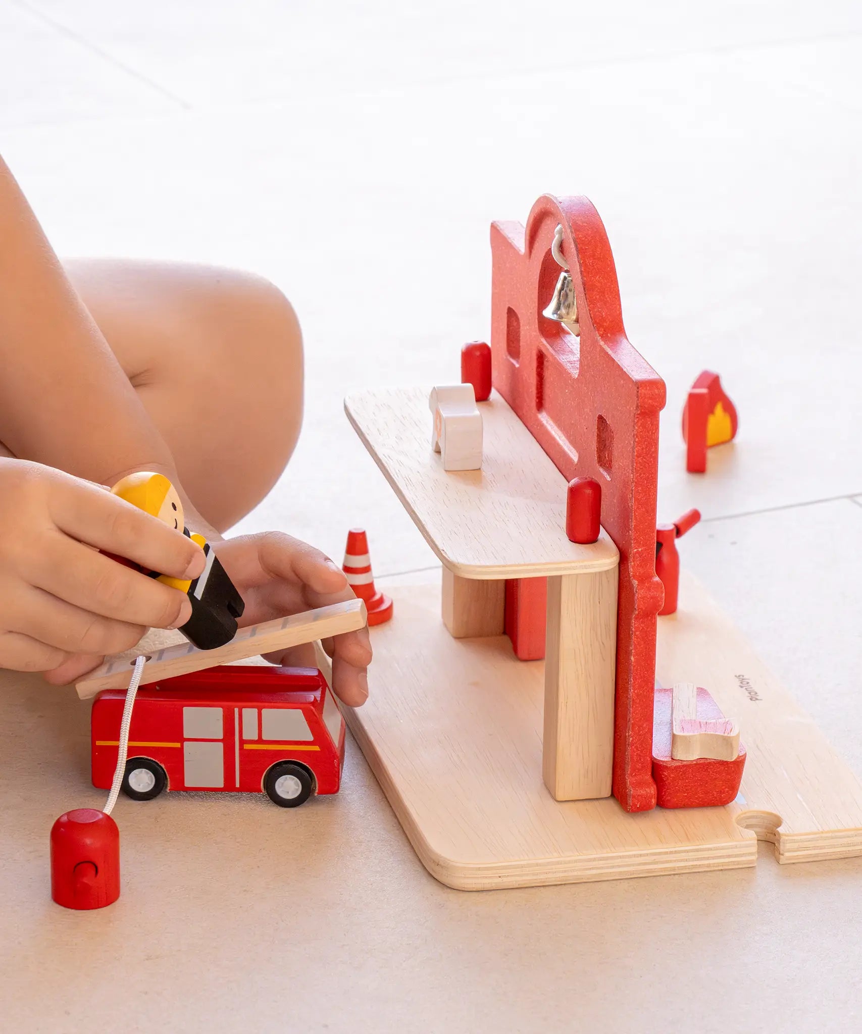 Child playing with the PlanToys fireman figure and fire engine next to the fire station.