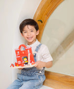 Child holding a PlanToys wooden fire station set with figures showing scale