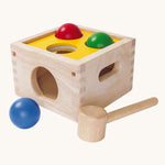 This PlanToys Punch and Drop game is a classic wooden pounding toy that babies and toddlers love – use the hammer to gently whack the three coloured balls through the holes in the wooden box and watch as they roll out. The ball colours are blue, red and green, and the top of the pounding box is yellow. The image is on a cream background