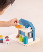 Back of Child playing with the PlanToys wooden blue house set showing the wooden furniture and family figures