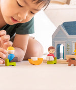 PlanToys wooden blue house set showing a child picking up a wooden father figure 