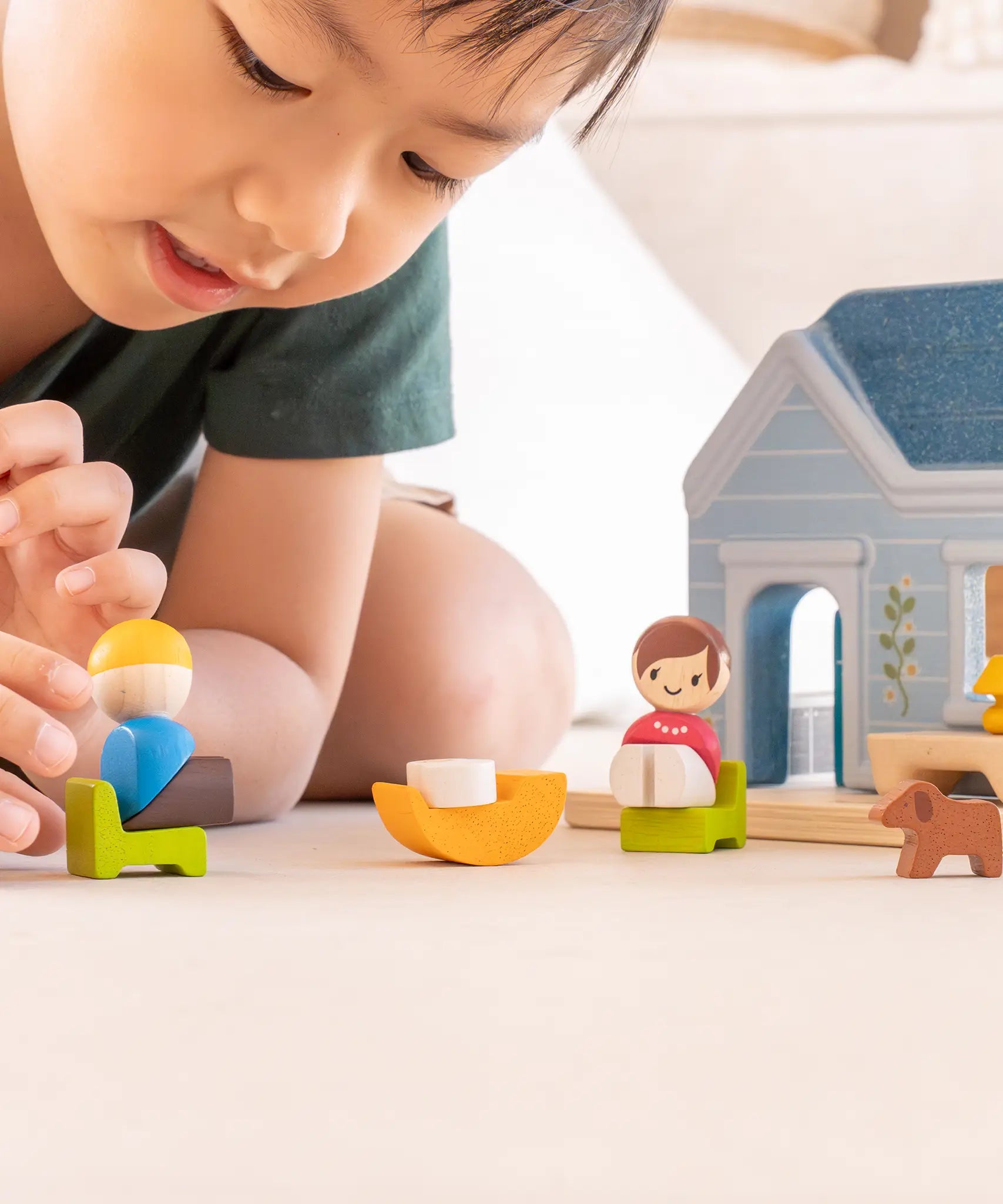 PlanToys wooden blue house set showing a child picking up a wooden father figure 