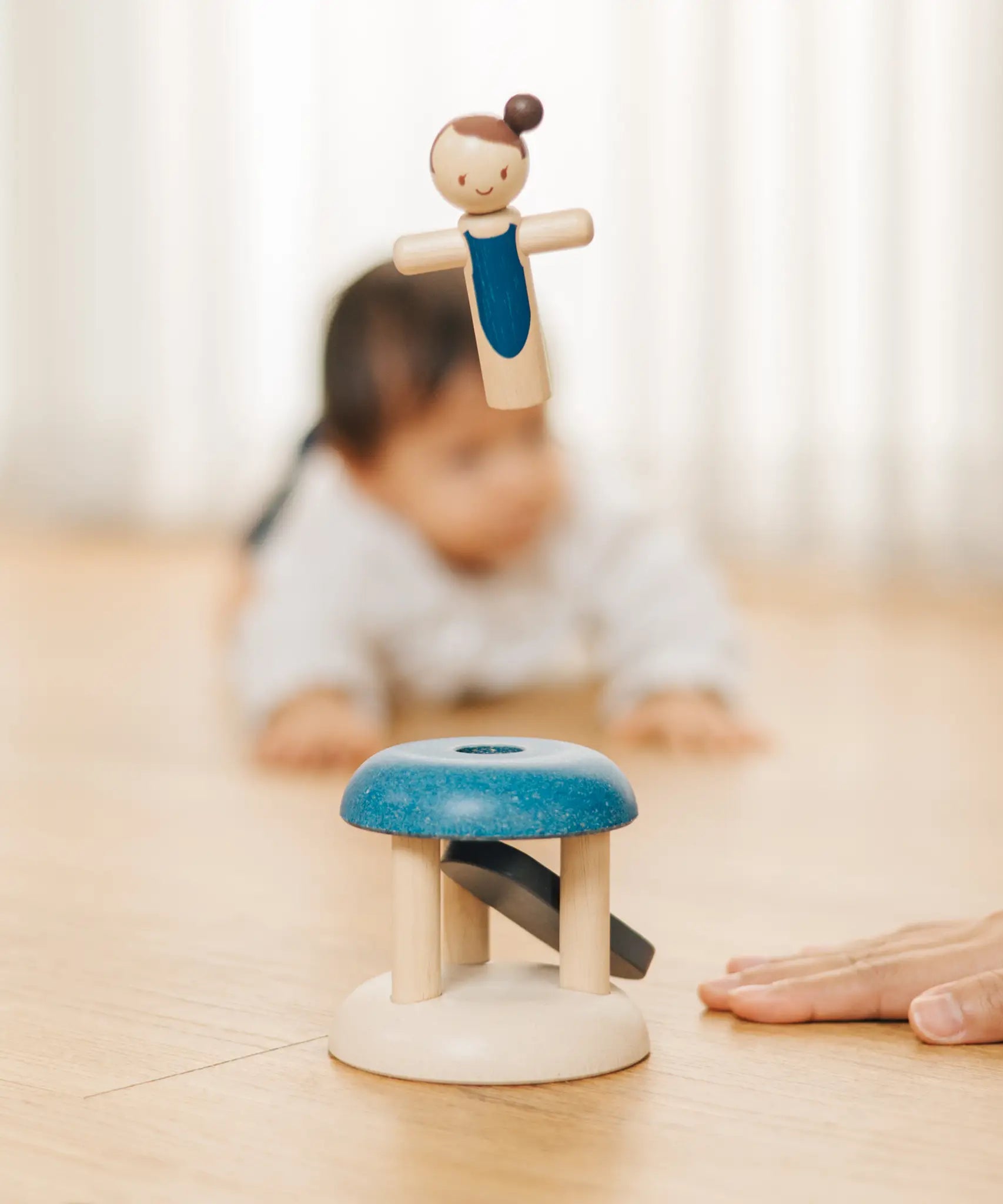 Adult hand pressing down on the base launching the PlanToys gymnast peg doll