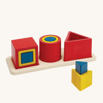 PlanToys Matching & Nesting Shapes Puzzle, is a fun wooden learning and educational toy for children. In the image are 3 square blocks inside each other, 3 circle blocks inside each other and 3 triangle block, with one on the wooden base and two in front stacked on each other. The colours of the blocks are red, yellow and blue, and are on a cream background 