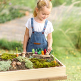 Child standing over a PlanToys seedling patch planter full of wooden veg piece in the garden