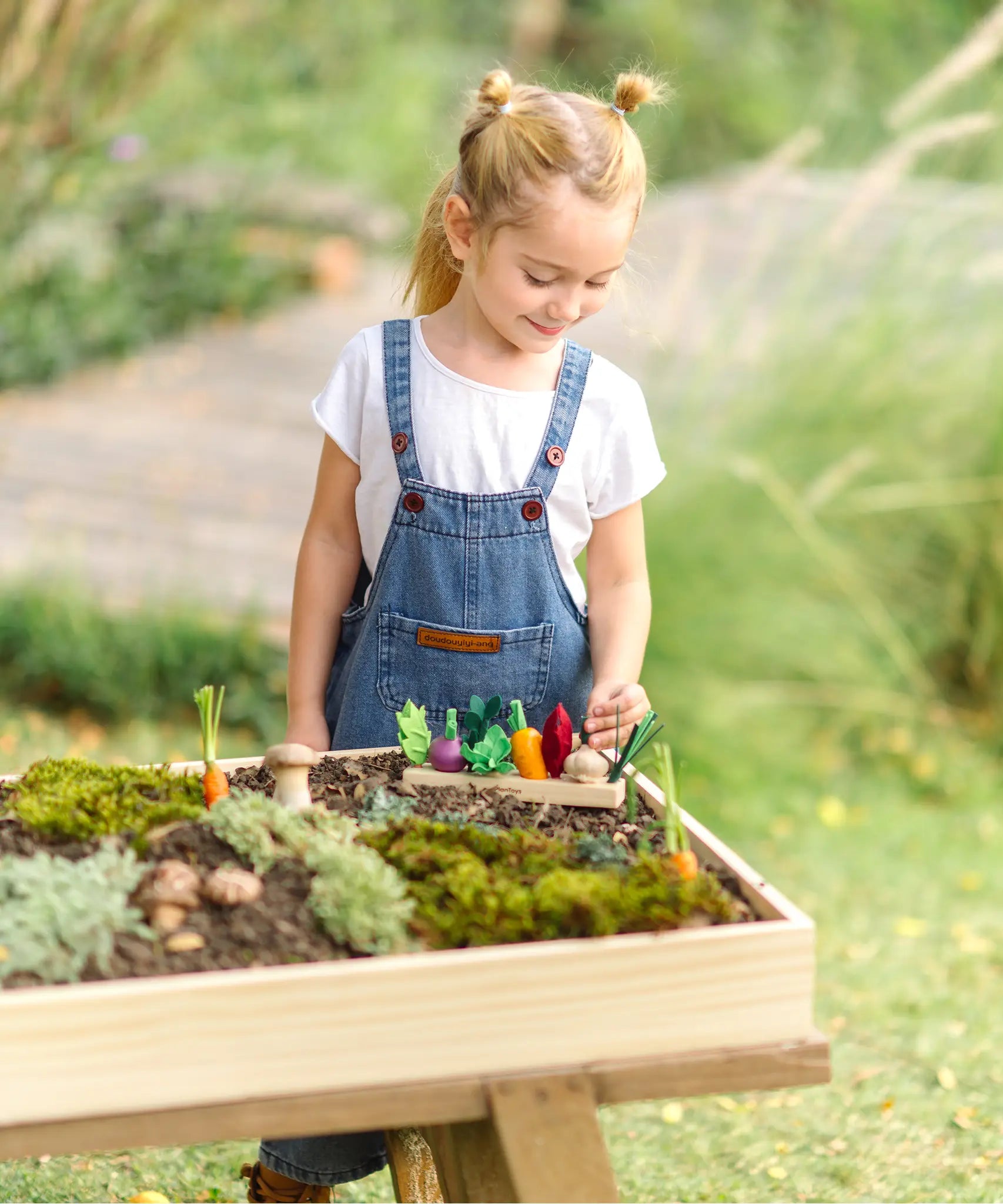Child standing over a PlanToys seedling patch planter full of wooden veg piece in the garden