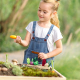 PlanToys wooden seedling planter with veg sitting on top and a child picking up a loose carrot veg piece