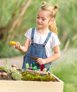 PlanToys wooden seedling planter with veg sitting on top and a child picking up a loose carrot veg piece