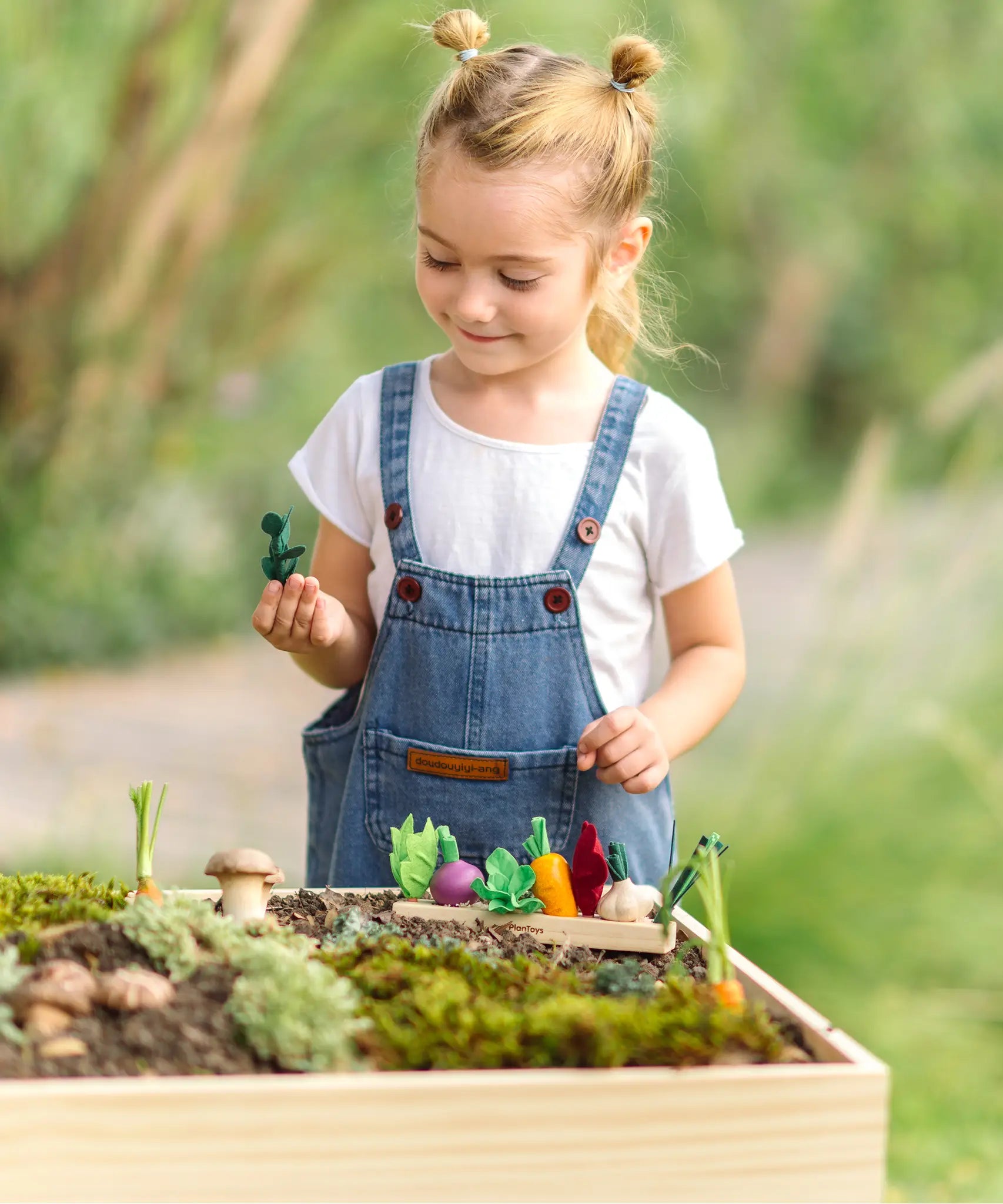 PlanToys wooden seedling planter with veg sitting on top and a child picking up a loose felted veg piece