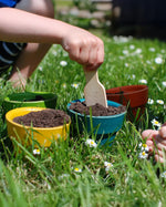 Plantoys wooden kids plant pots filled with soil by a child in a garden.