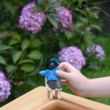 A child holding a doll from the PlanToys doll house family set in their hand. The child is placing it on a wooden toy seat.