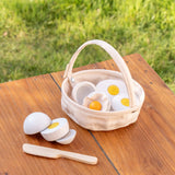 A Plantoys basket with wooden eggs to cut standing on a wooden table 