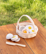 A Plantoys basket with wooden eggs to cut standing on a wooden table 