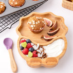 Eco Rascals Dinosaur Bamboo Suction Plate with a muffin, fig slices, yogurt and fresh fruit, and purple silicone and bamboo baby spoon.