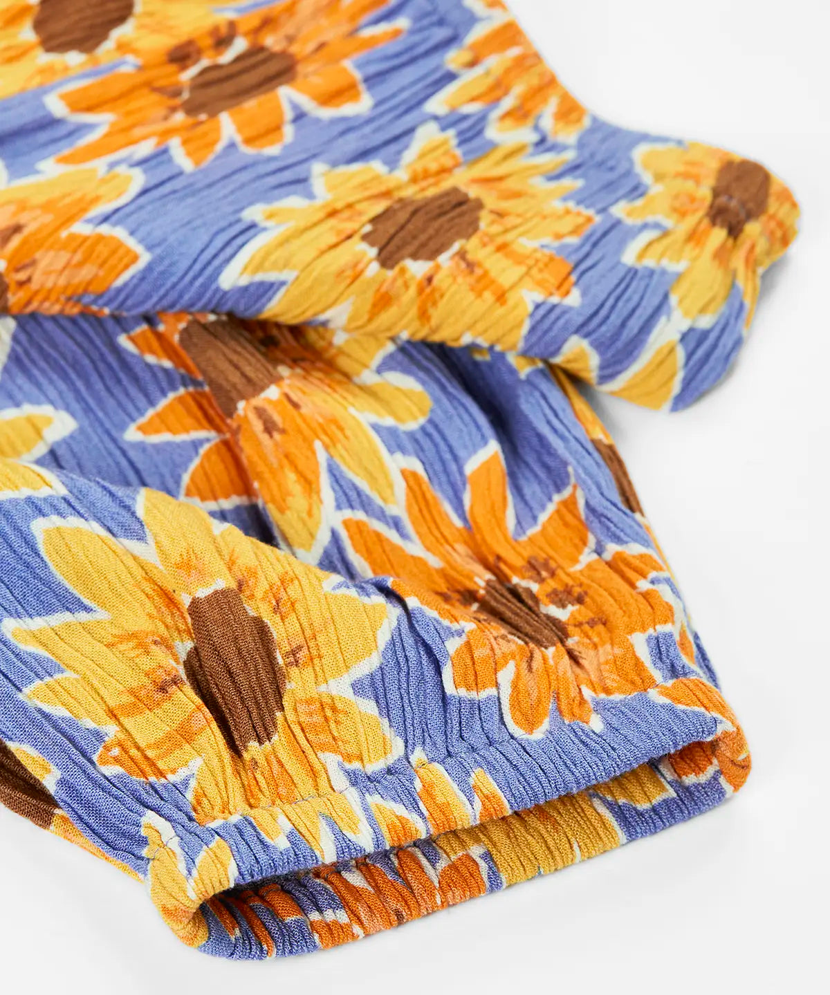 Frugi Lowenna jumpsuit in purple with a repeating sunflower print laid flat showing elasticated leg cuffs