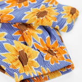 Frugi Lowenna jumpsuit in purple with a repeating sunflower print laid flat showing elasticated leg cuffs