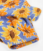 Frugi Lowenna jumpsuit in purple with a repeating sunflower print laid flat showing elasticated leg cuffs