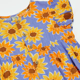 Frugi Lowenna jumpsuit in purple with a repeating sunflower print laid flat. Showing frilled shoulder and front button fasteners