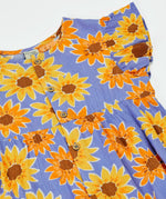 Frugi Lowenna jumpsuit in purple with a repeating sunflower print laid flat. Showing frilled shoulder and front button fasteners